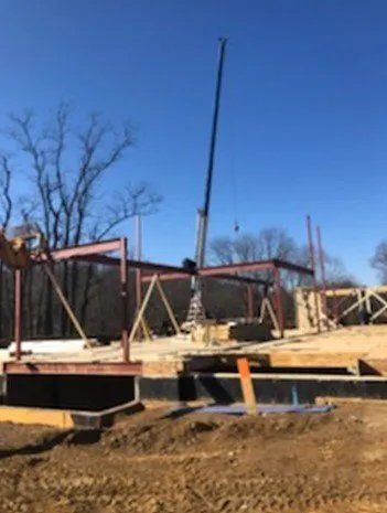 Construction site with a crane lifting a steel beam for a building frame. Bright blue sky.
