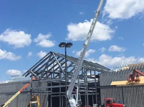 Construction site with crane lifting metal beams for a building frame against a blue sky with clouds.
