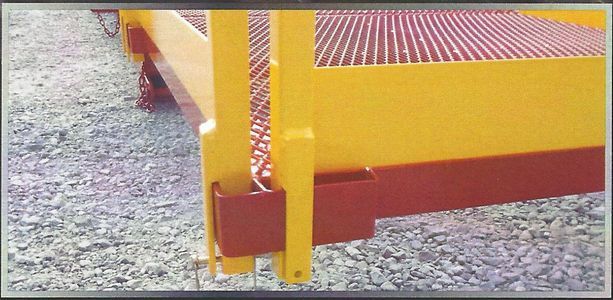 A yellow and red metal structure with a gridded platform, set on a gravel surface.
