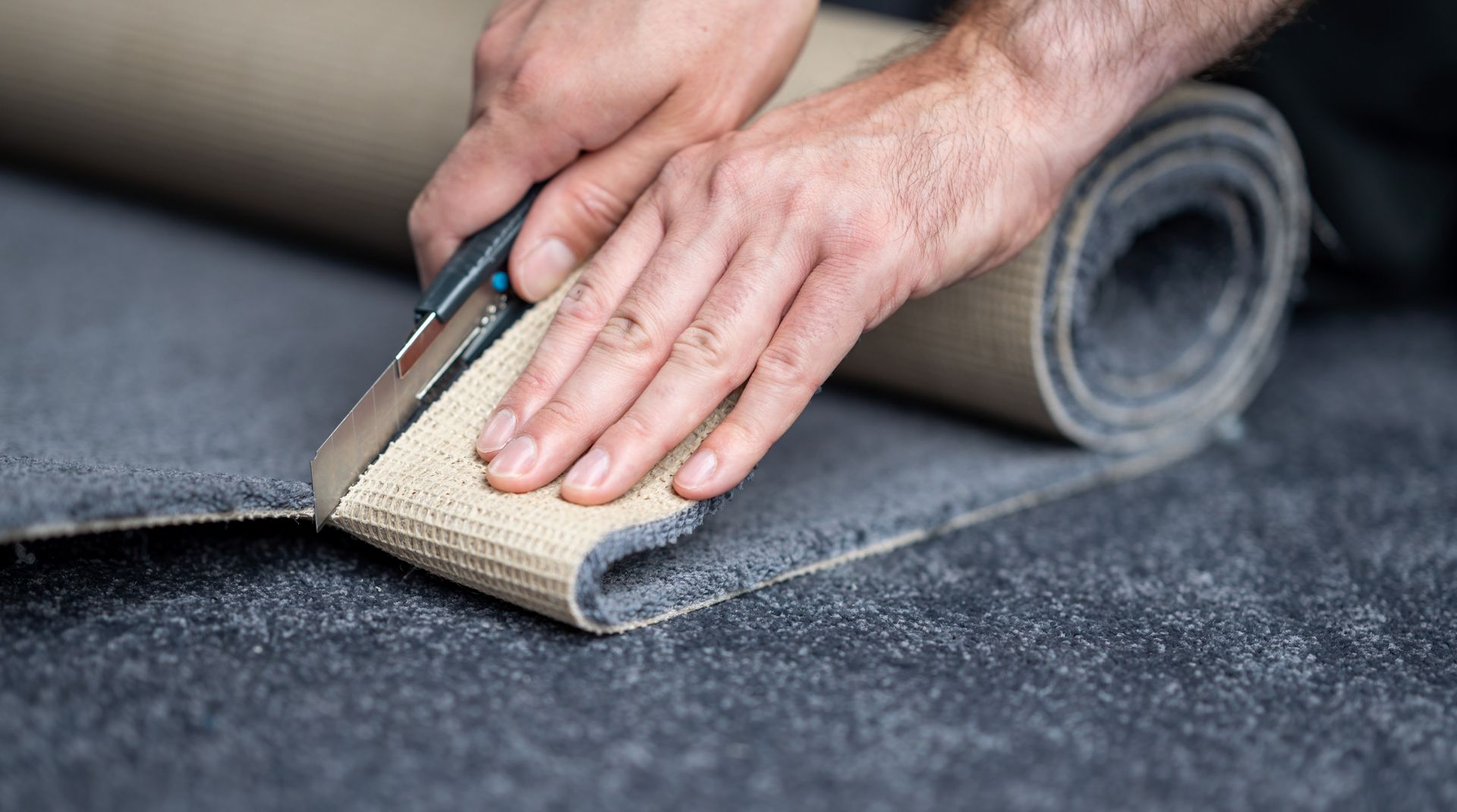 A person is cutting a roll of carpet with a pair of scissors.