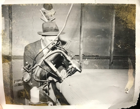 A black and white photo of a man in a hat working on a machine