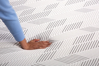 A person is touching a mattress with their hand