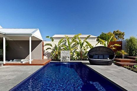 Backyard with a rectangular pool, cabana, and a round outdoor sofa on a sunny day.