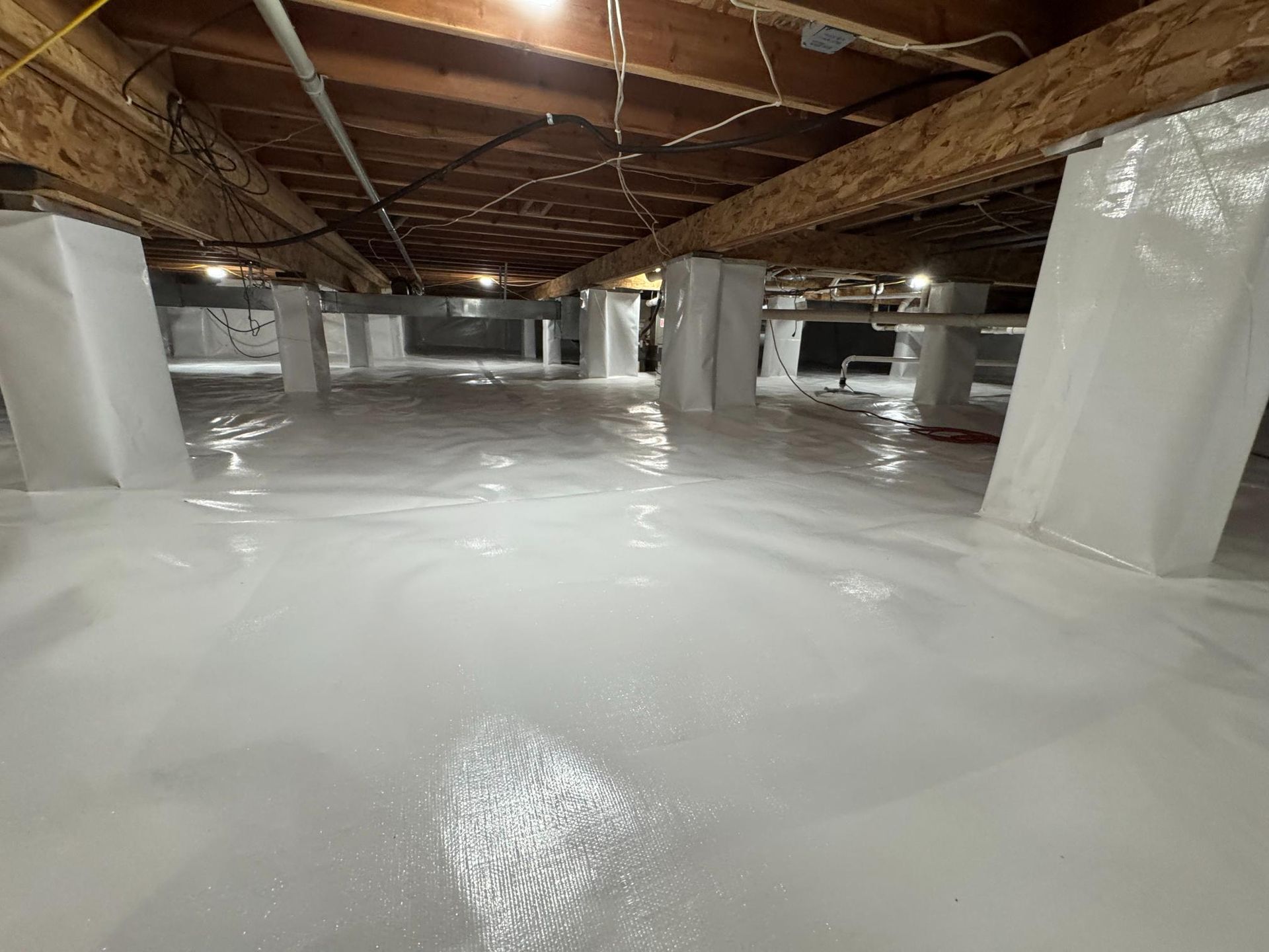 A crawl space encapsulated with white vapor barrier plastic covering the floor and the structural support piers.