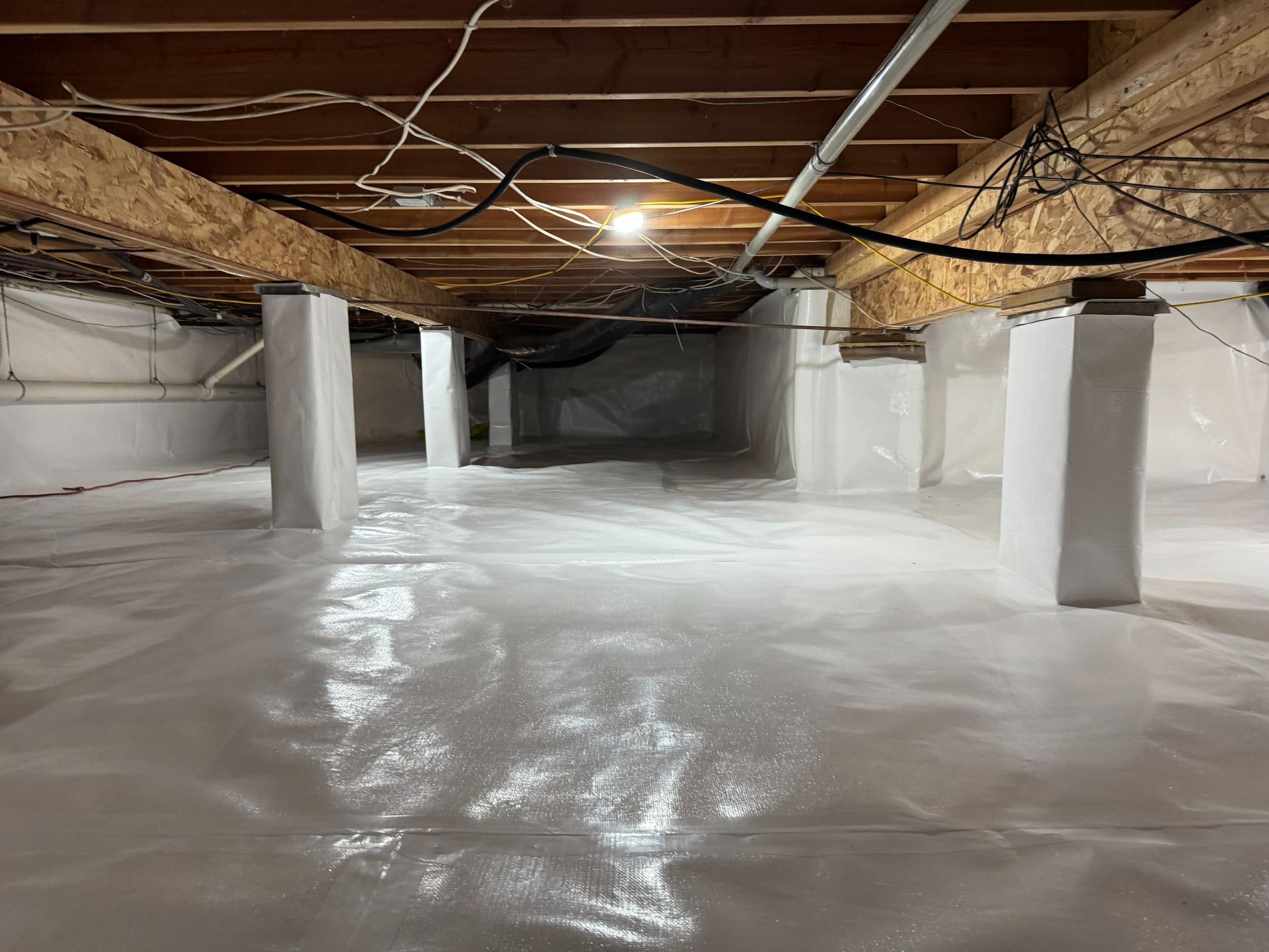 A crawlspace featuring a white vapor barrier covering the floor and wrapping around the vertical support pillars.