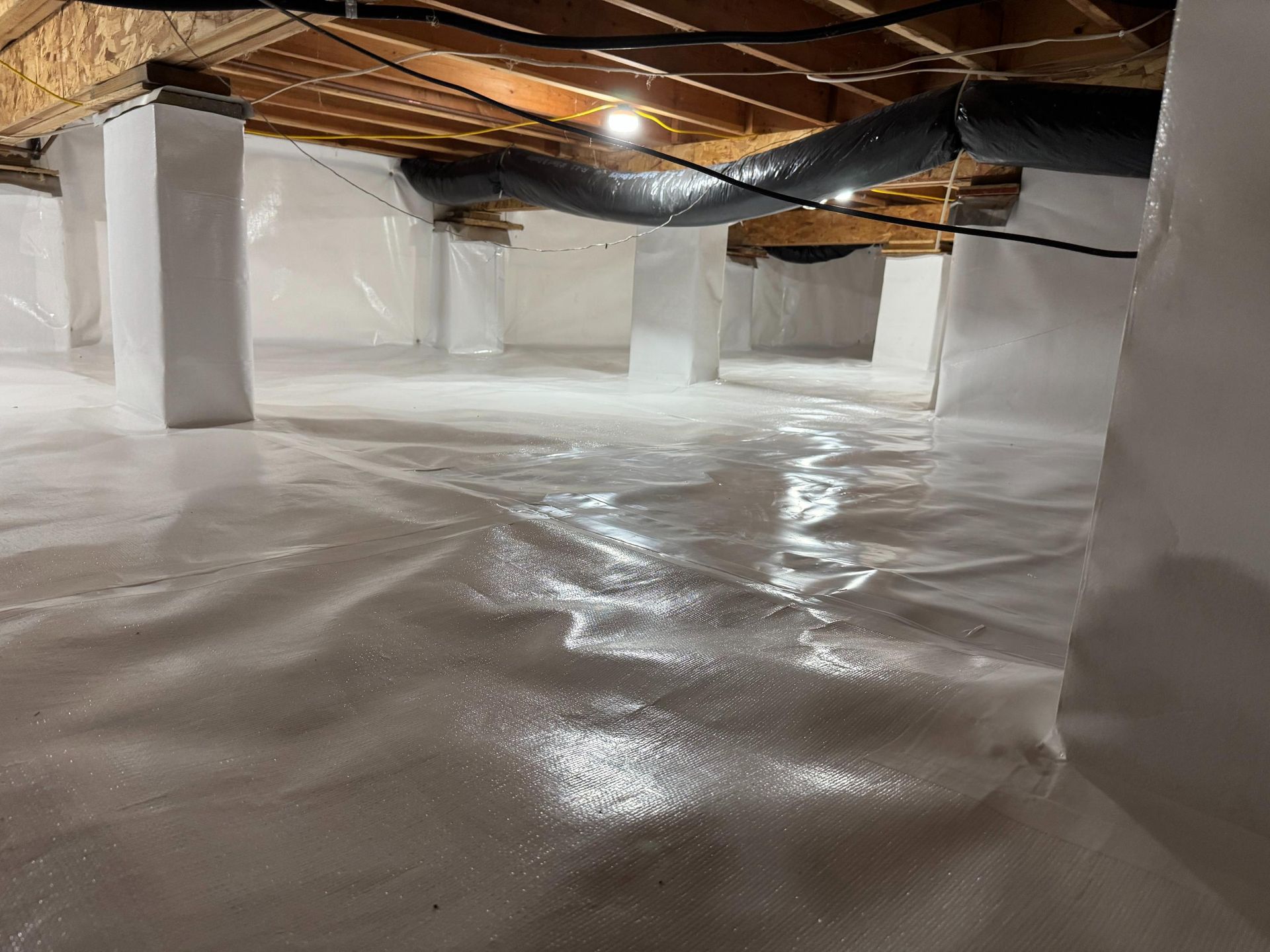 A clean crawl space encapsulated with white vapor barrier plastic and white-wrapped structural support pillars.
