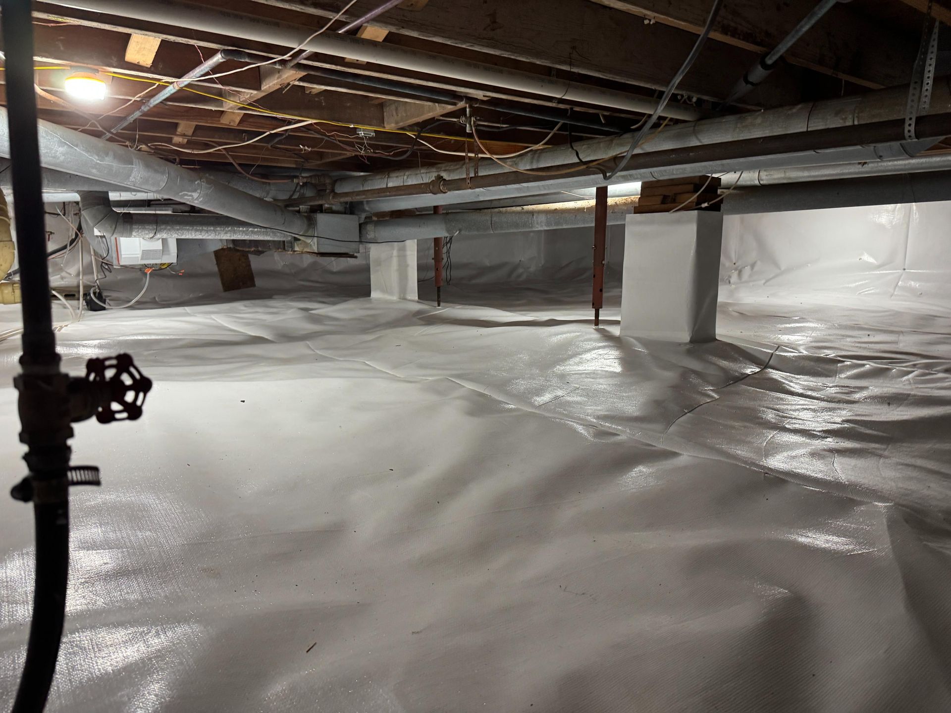 A crawl space with a clean white vapor barrier covering the floor and white pillars supporting the wooden joists above.