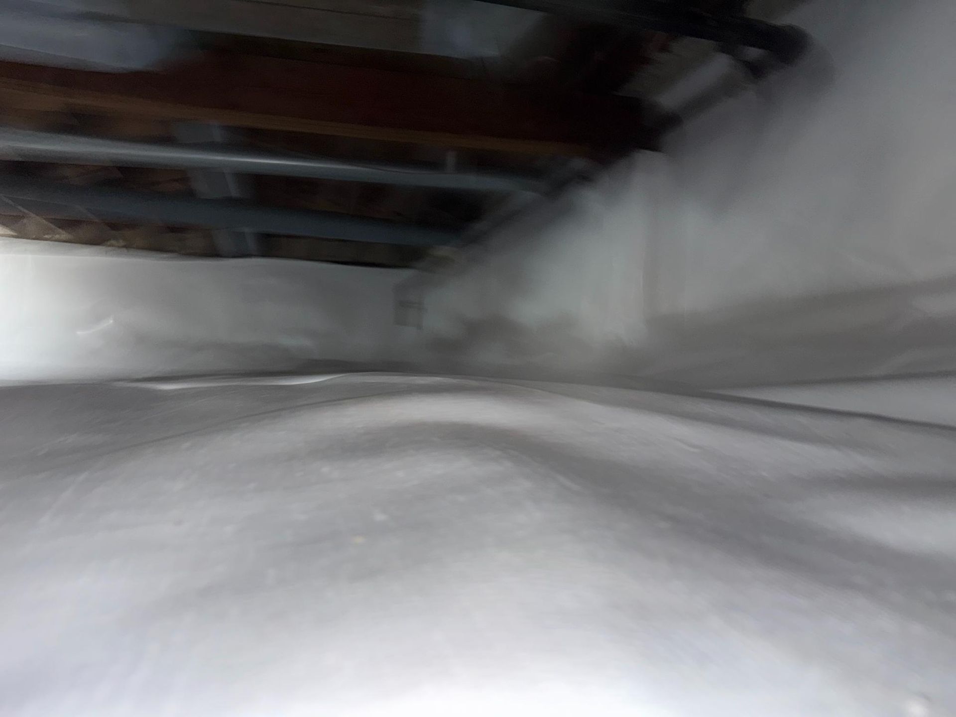 A crawl space with a clean white vapor barrier covering the floor and foundation walls beneath wooden floor joists.