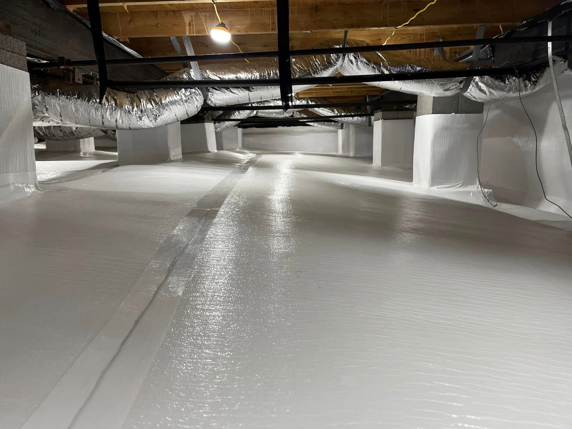 A clean, encapsulated crawlspace with white vapor barriers covering the ground, walls, and pillars under floor joists.