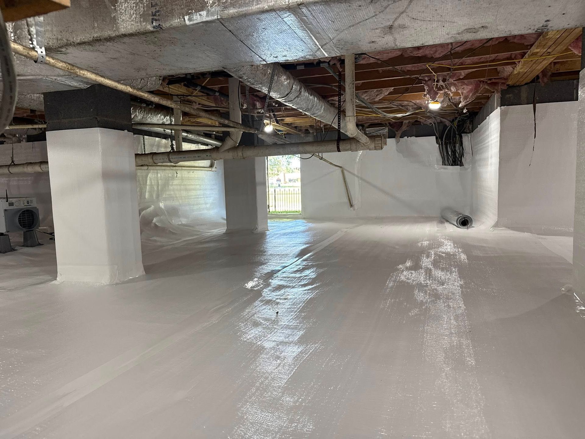 A crawl space encapsulated with white vapor barrier plastic covering the floor, foundation walls, and support pillars.