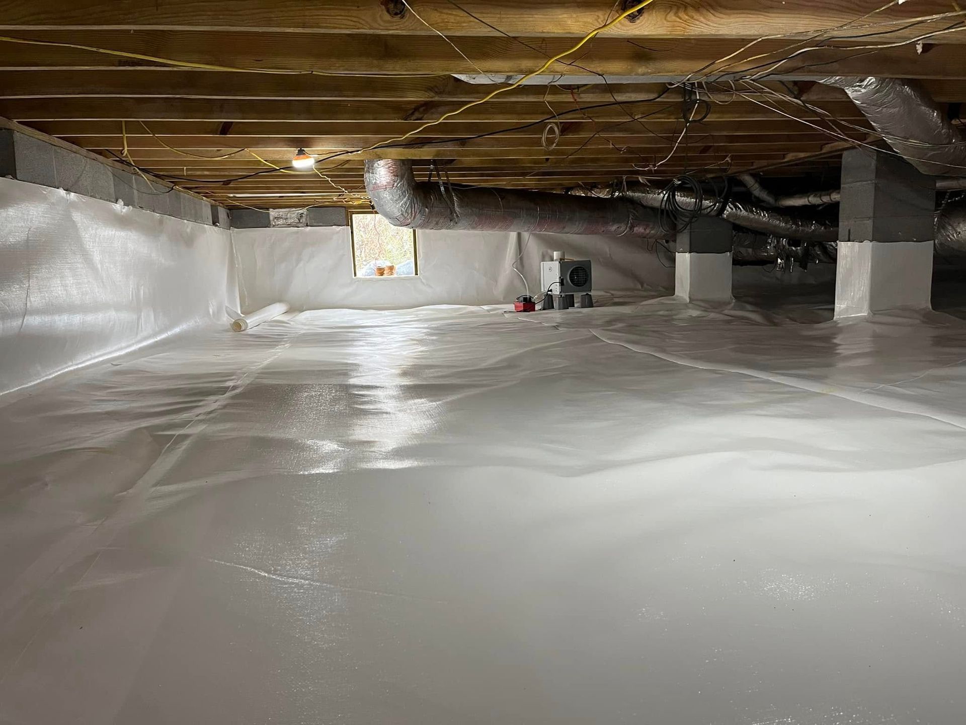 A crawl space encapsulated with white vapor barrier, wooden floor joists, and HVAC ductwork visible above.