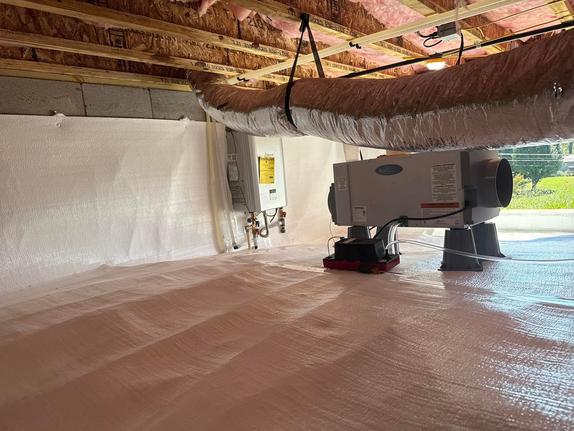 A crawl space with insulated walls, a vapor barrier on the floor, an HVAC unit, and flexible ductwork hanging from joists.