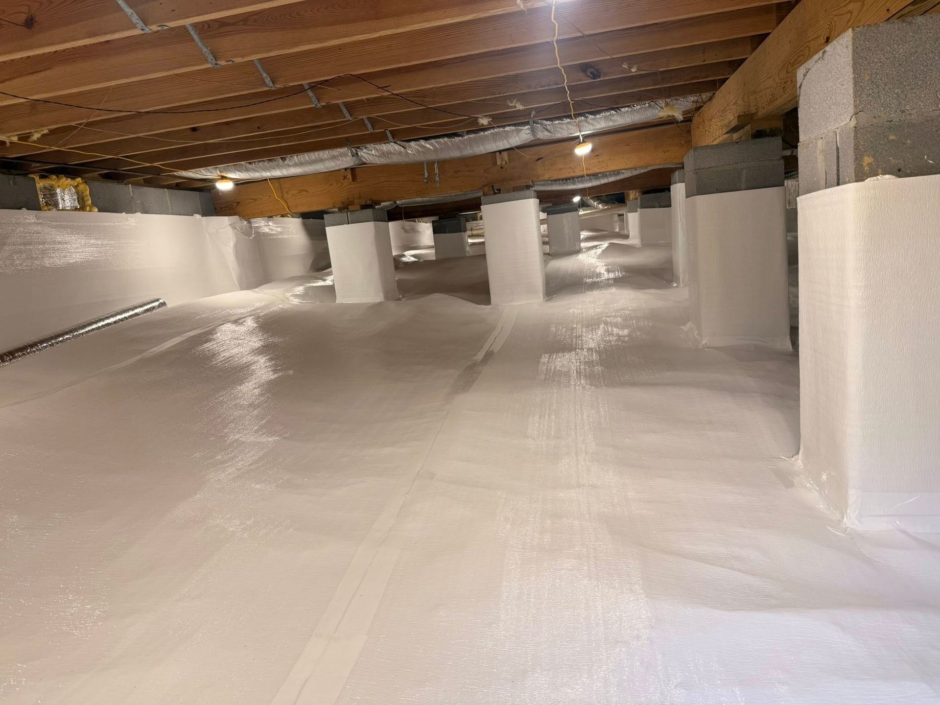 A crawl space with white moisture barrier lining the floor and wrapping around the concrete support pillars.