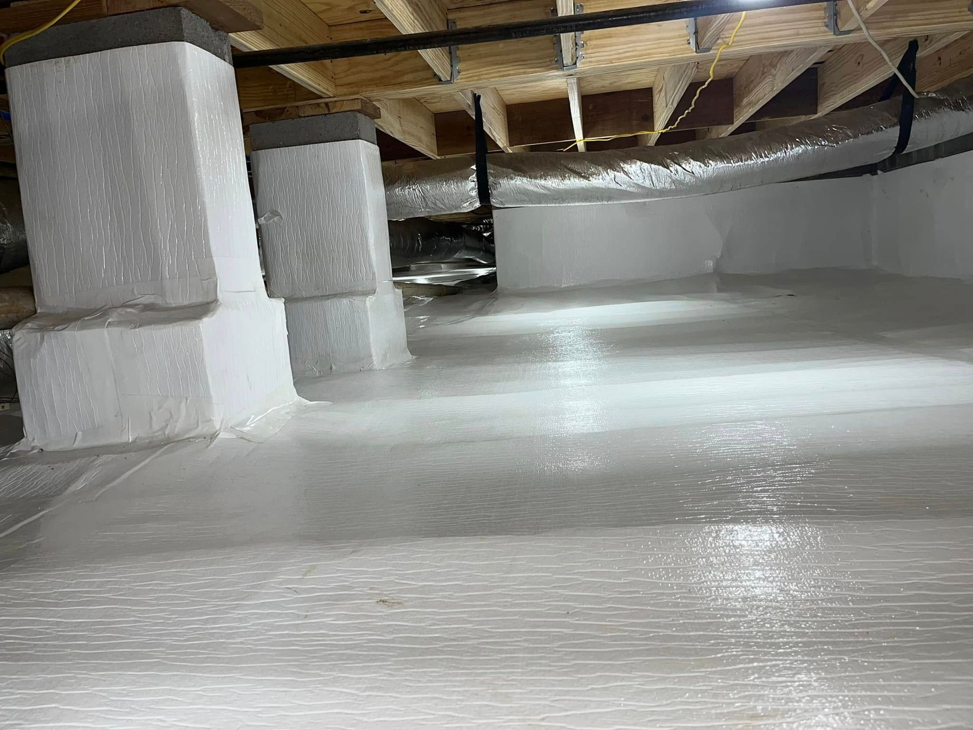 A crawl space featuring a white vapor barrier covering the floor and wrapping around concrete support pillars.