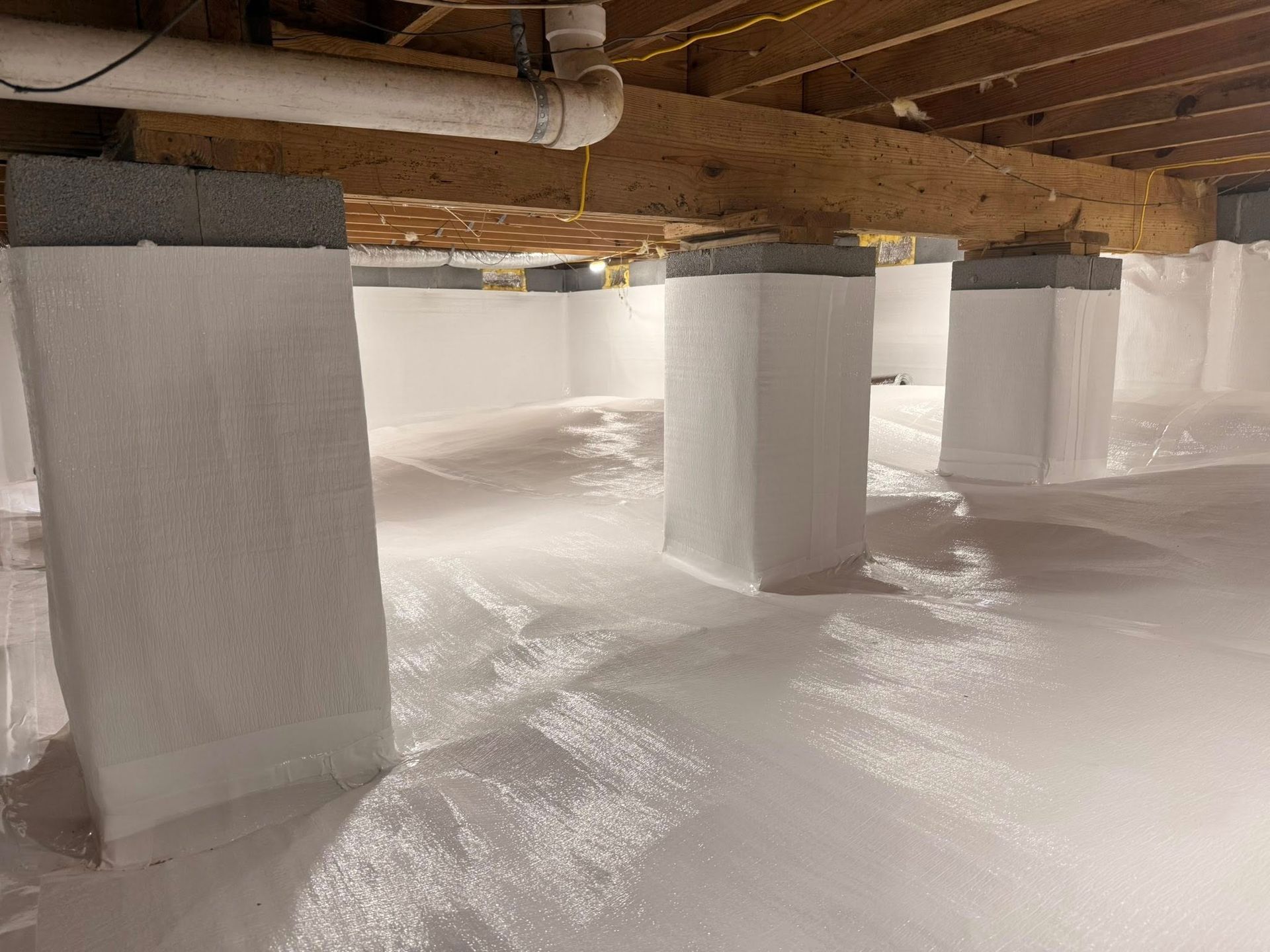 A clean, encapsulated crawlspace with white vapor barriers covering the ground and structural support piers.