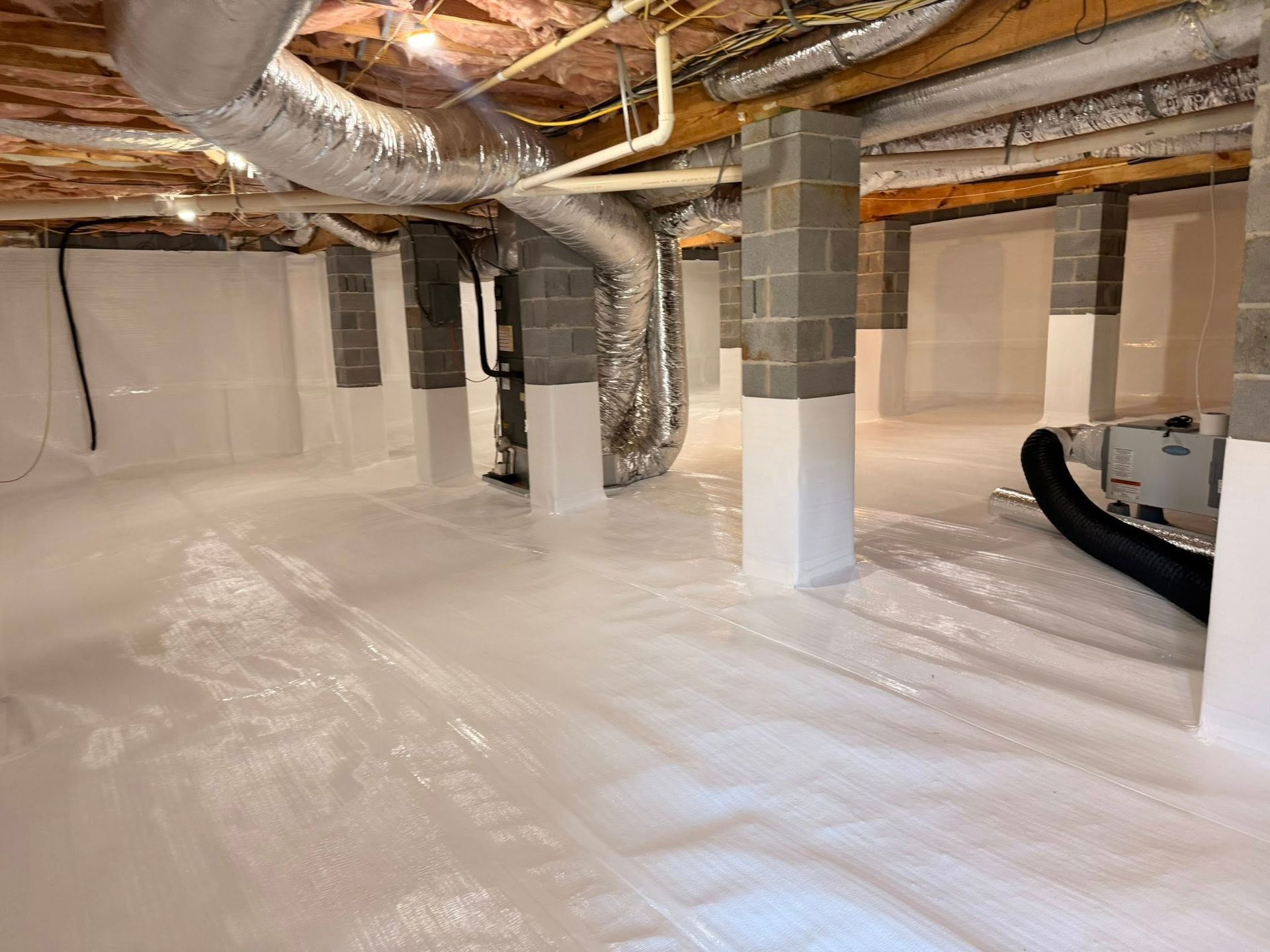 Crawl space with white vapor barrier, encapsulated foundation walls, supporting concrete pillars, and ventilation ducts.