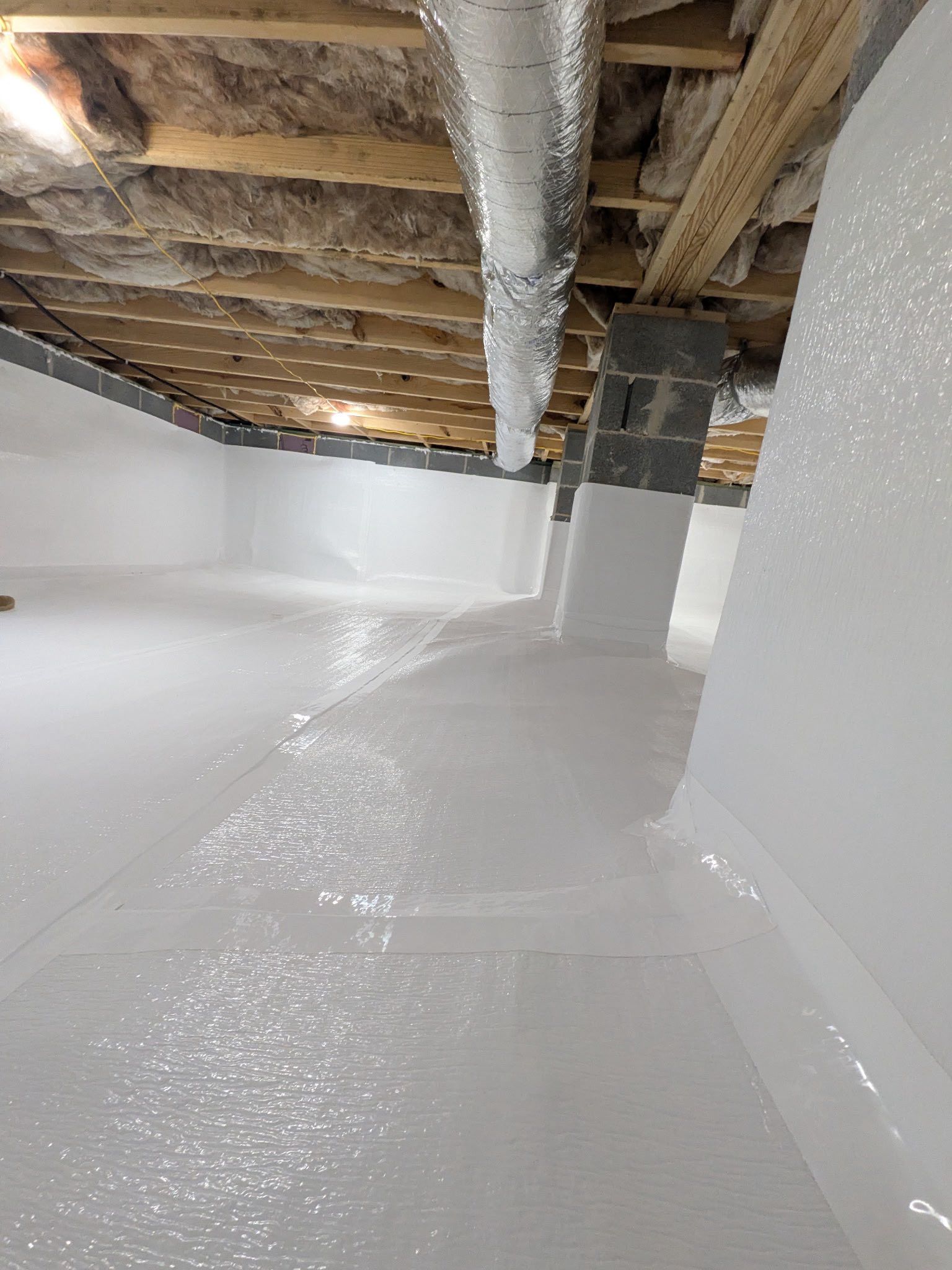 An unfinished basement with white-painted walls and floor, exposed wood ceiling joists, and a silver ventilation duct.