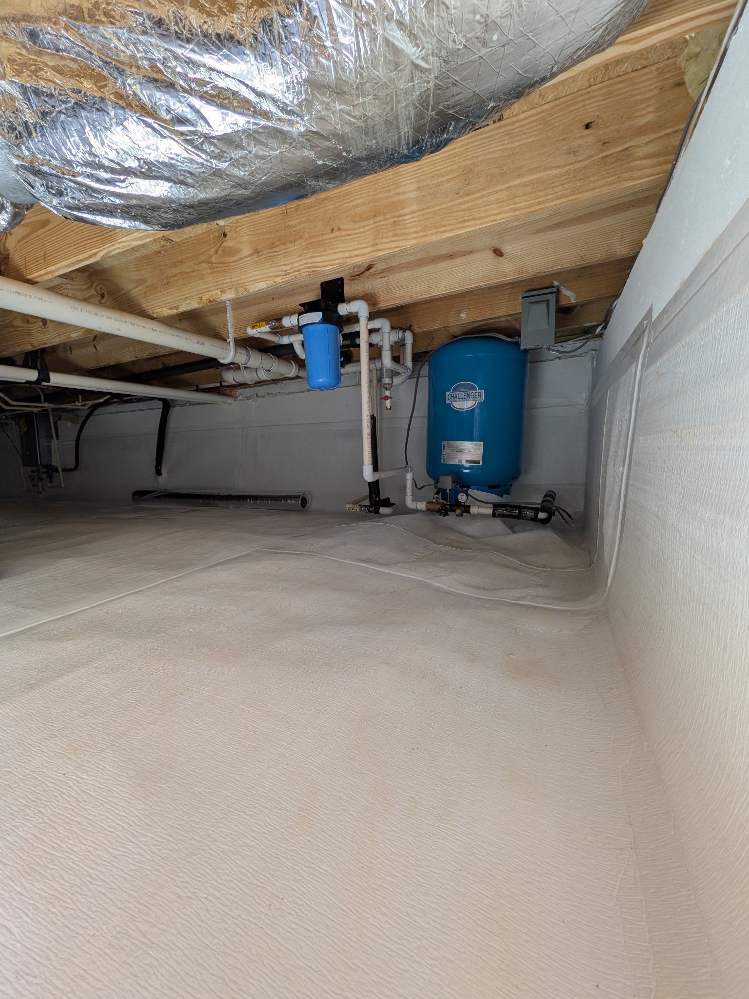 A blue water pressure tank and a small water filter mounted to floor joists in a crawl space with white liner.