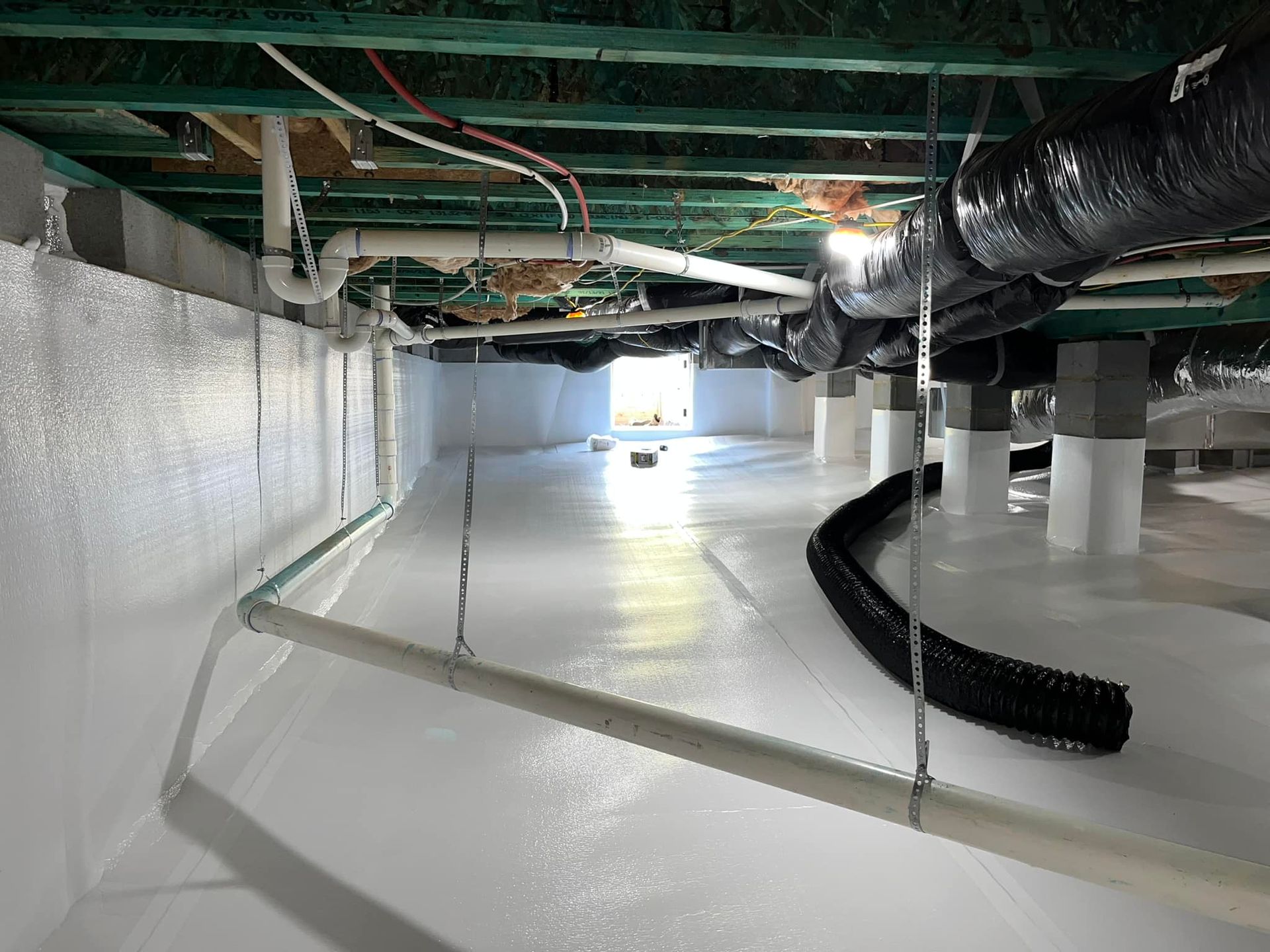 A crawl space encapsulated with white vapor barriers on the walls and floor, with visible plumbing and structural piers.