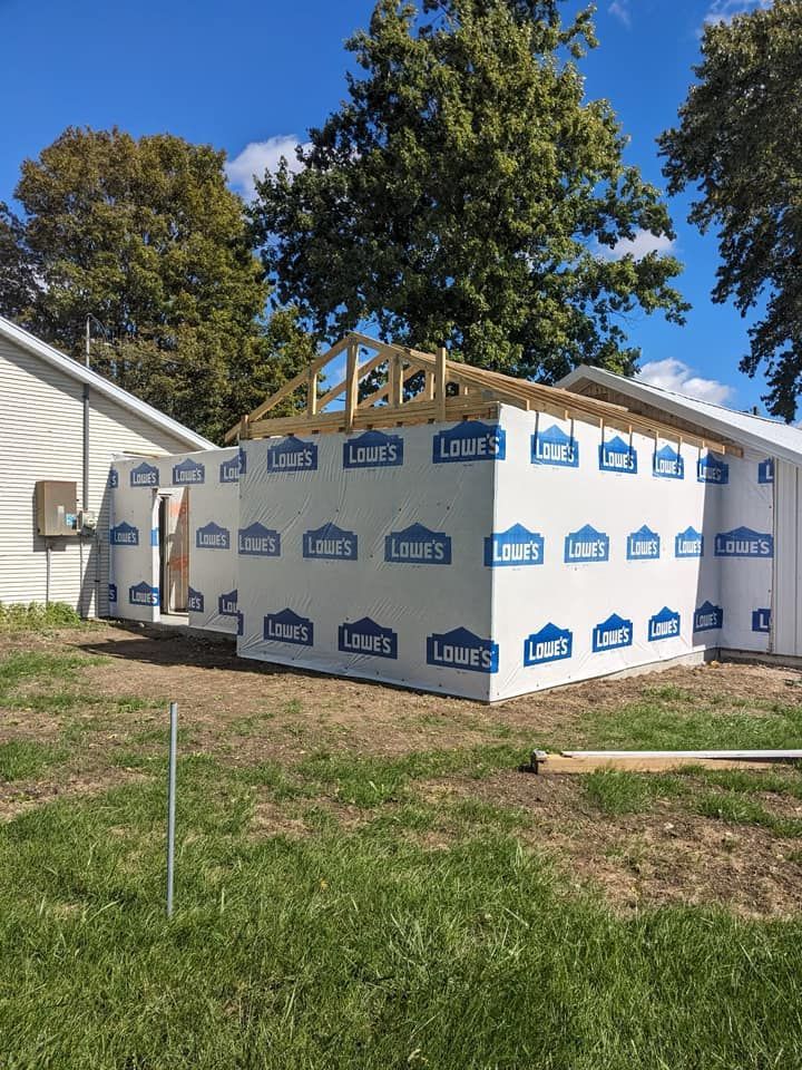 A structure under construction with a wooden roof frame and white walls wrapped in Lowe's branded protective house wrap.