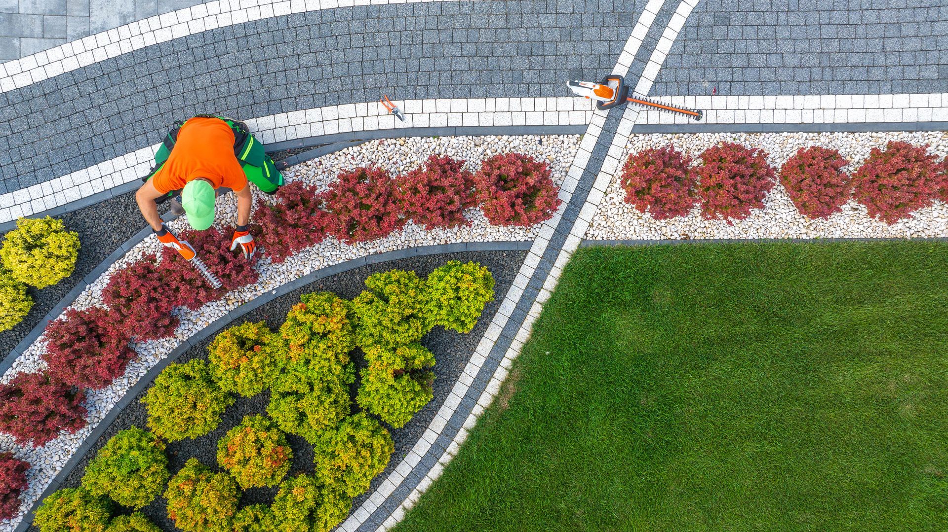 Overhead view: Gardener tending colorful flowerbeds surrounded by patterned paving.