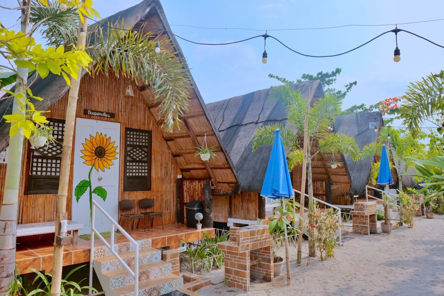 A row of wooden houses with umbrellas and a sunflower on the door.