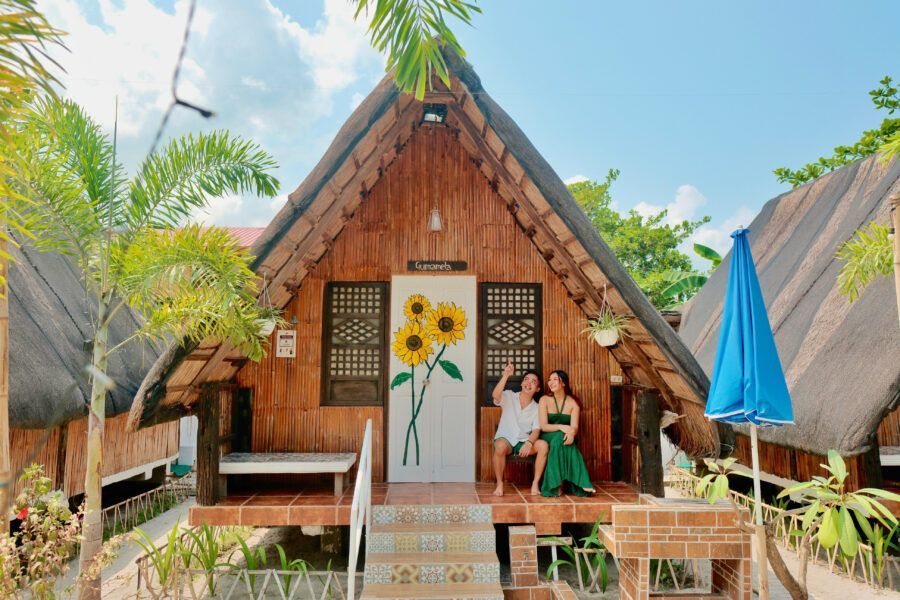 Two women are sitting on the porch of a small wooden house with sunflowers painted on the door.