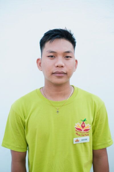 A young man in a green t-shirt is standing in front of a white wall.
