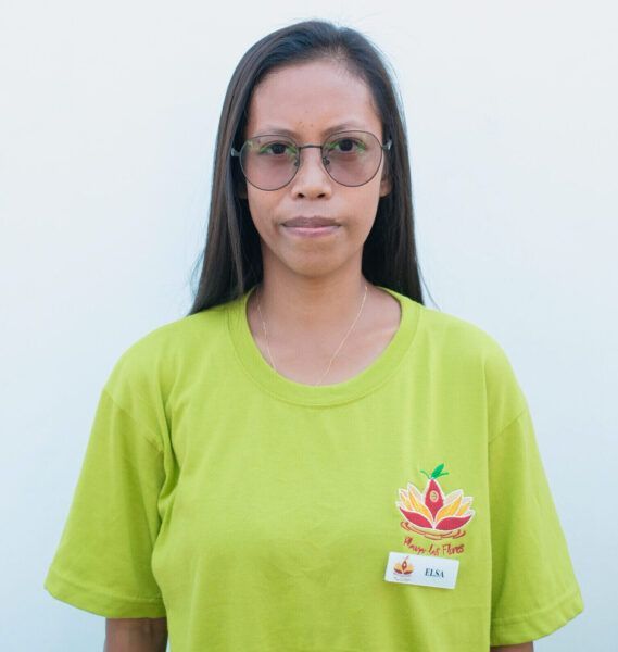 A woman wearing glasses and a green shirt is standing in front of a white wall.