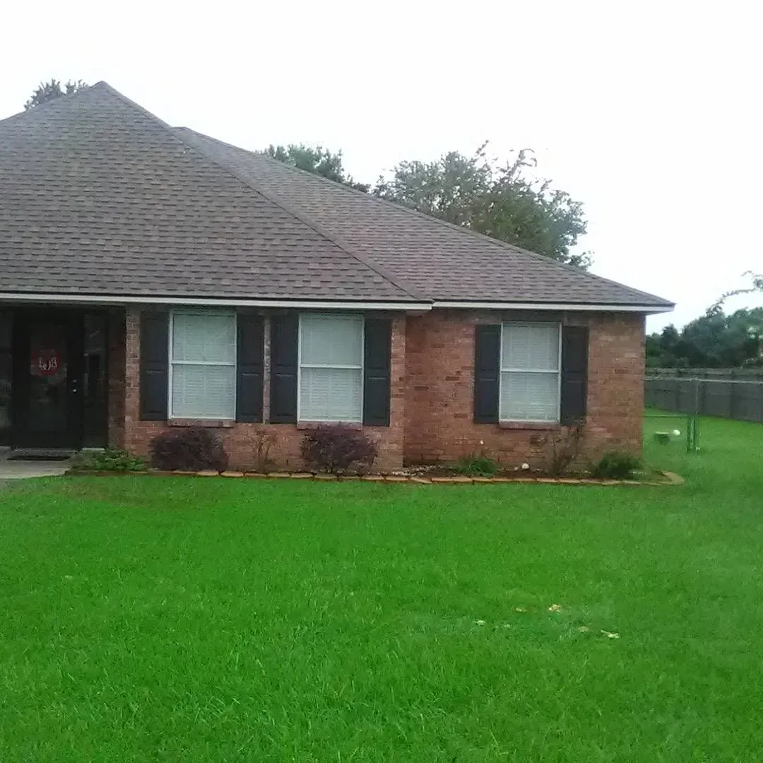 Brick house with green lawn and dark shutters.