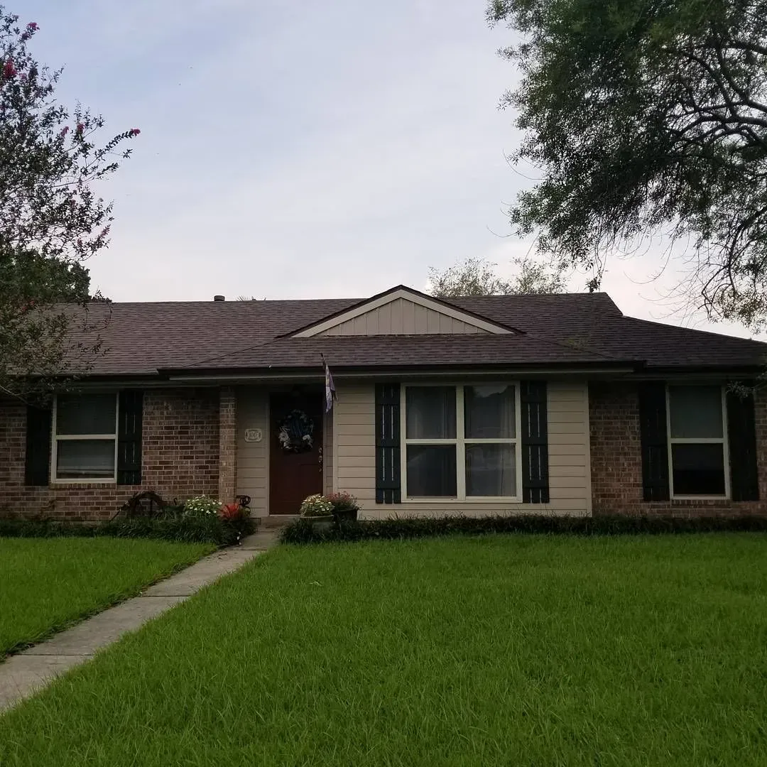 Brick house with tan siding, dark shutters, and a green lawn.