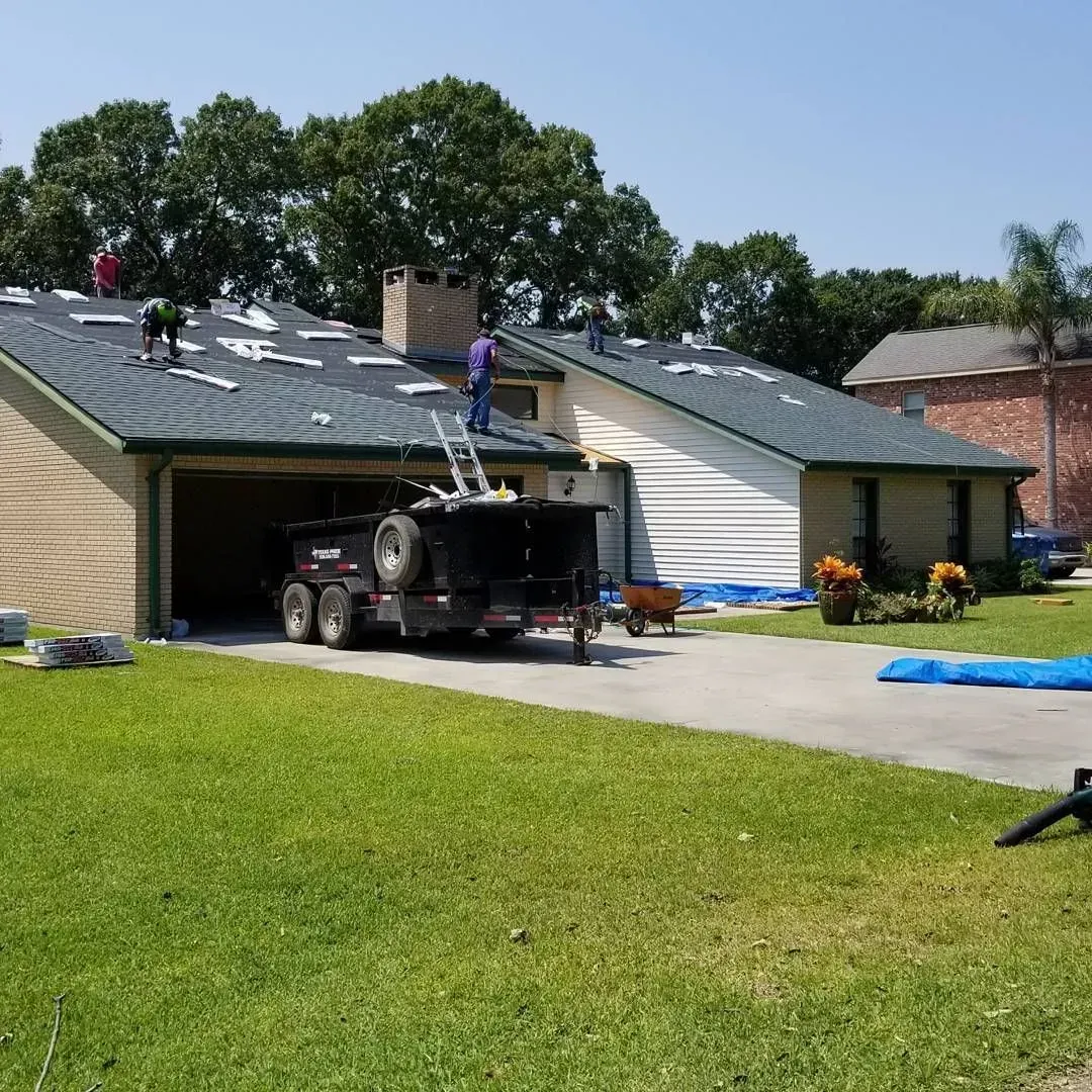 Roofing crew on a house roof, with a trailer parked in the driveway.