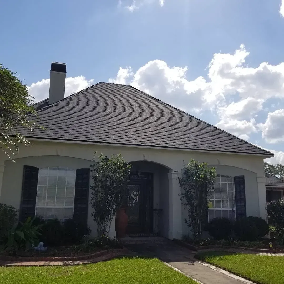 A light-colored house with a dark roof, black shutters, chimney, and cloudy sky.