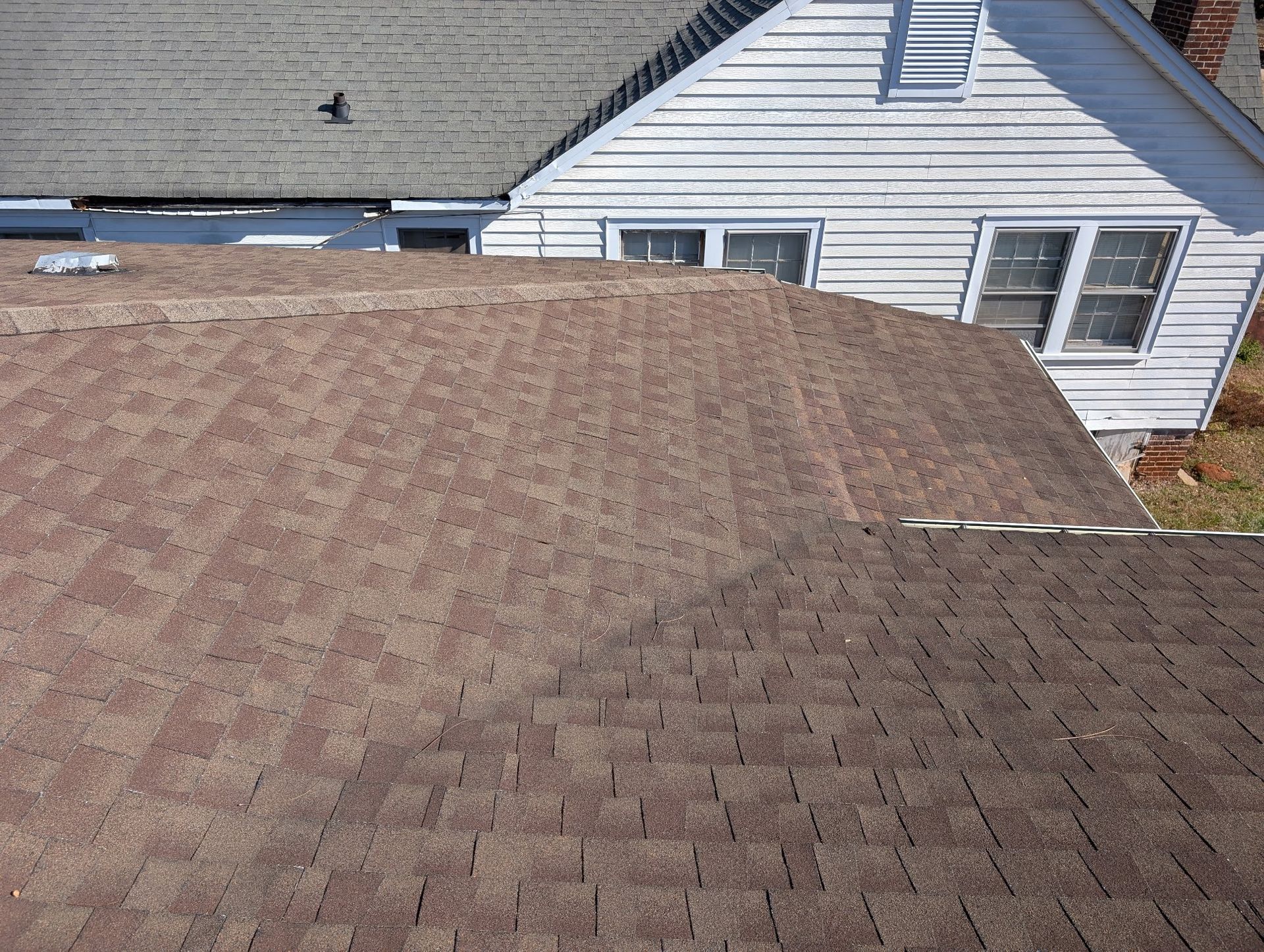 Brown asphalt shingle roof with a white house in the background.