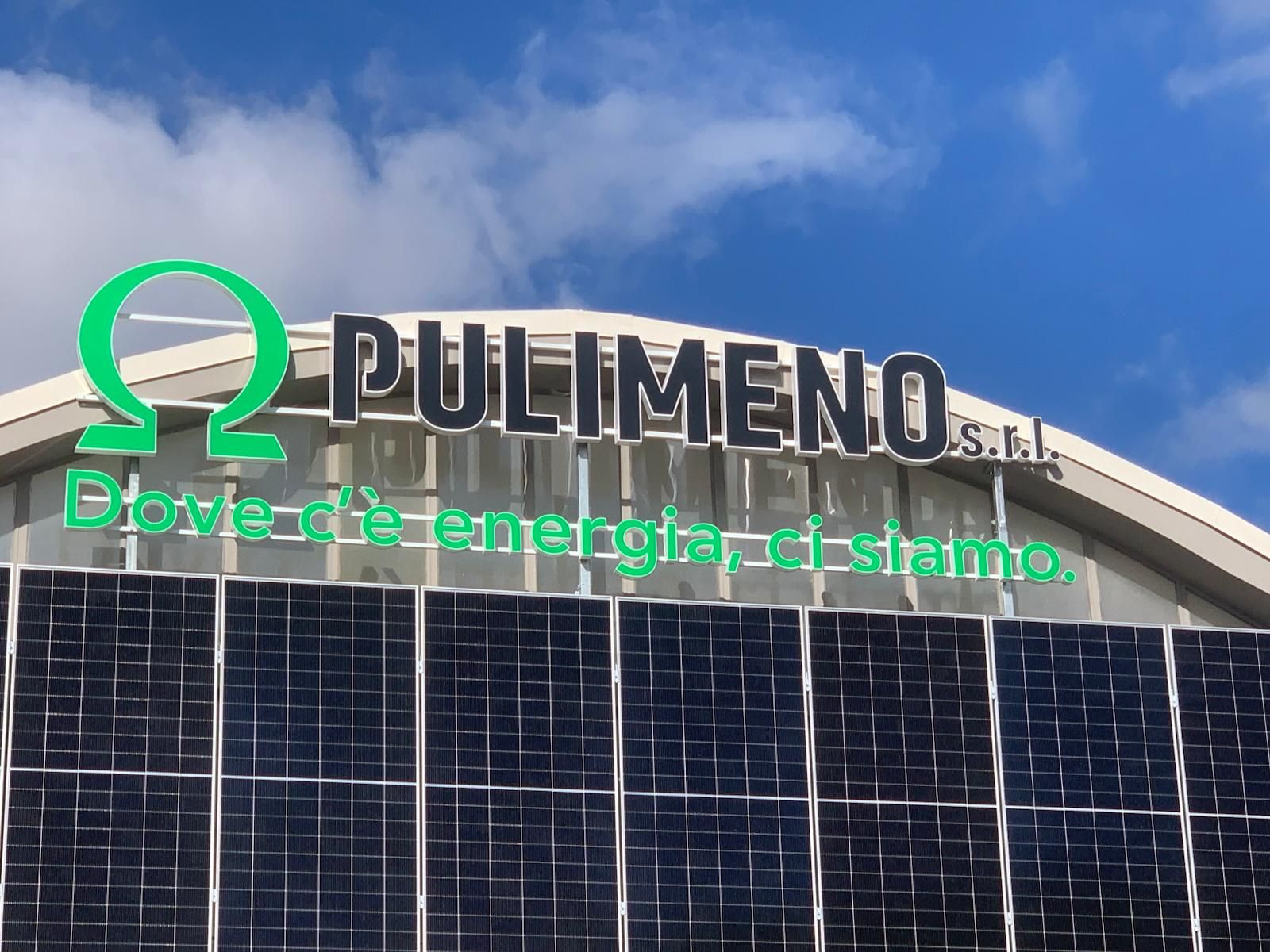 Edificio con pannelli solari e un cartello della Pulimeno srl contro un cielo azzurro.
