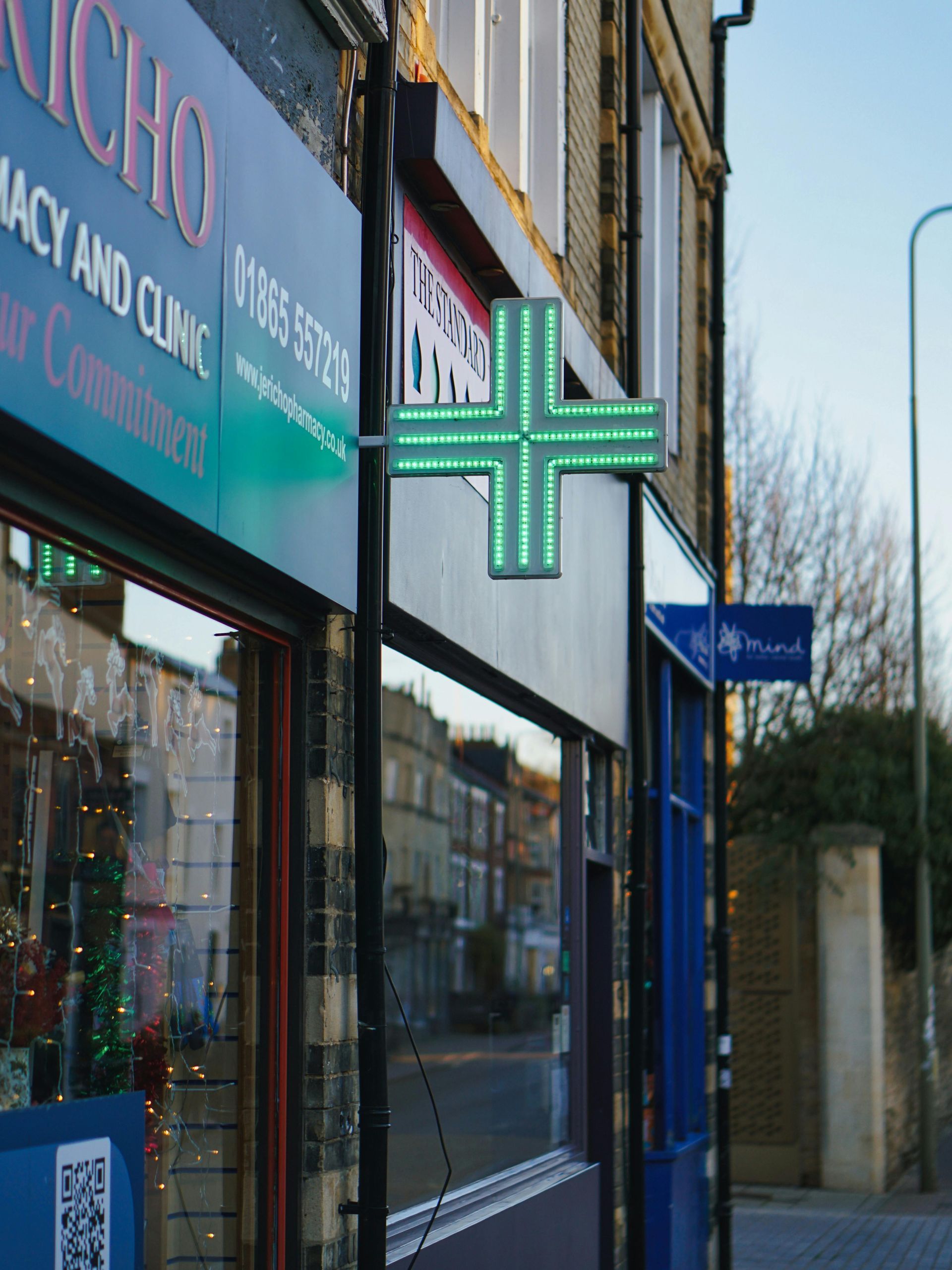 Vetrina della farmacia con un'insegna a forma di croce verde luminosa.