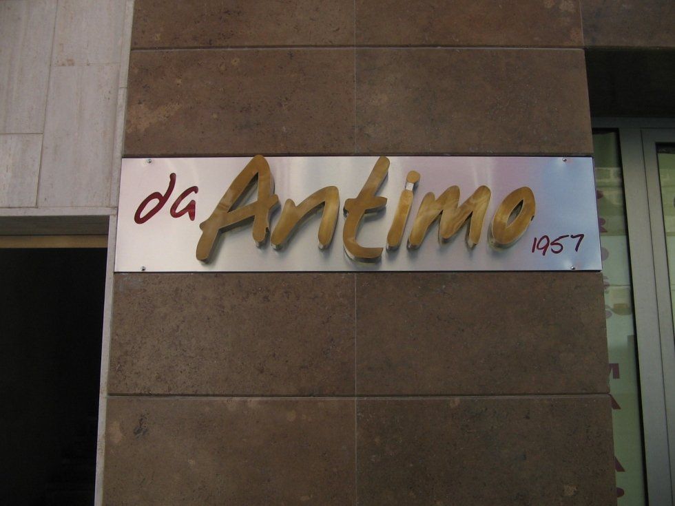 Insegna del ristorante "da Antimo", scritta dorata su una targa di metallo, incastonata in un muro di mattoni, con la scritta "1957".