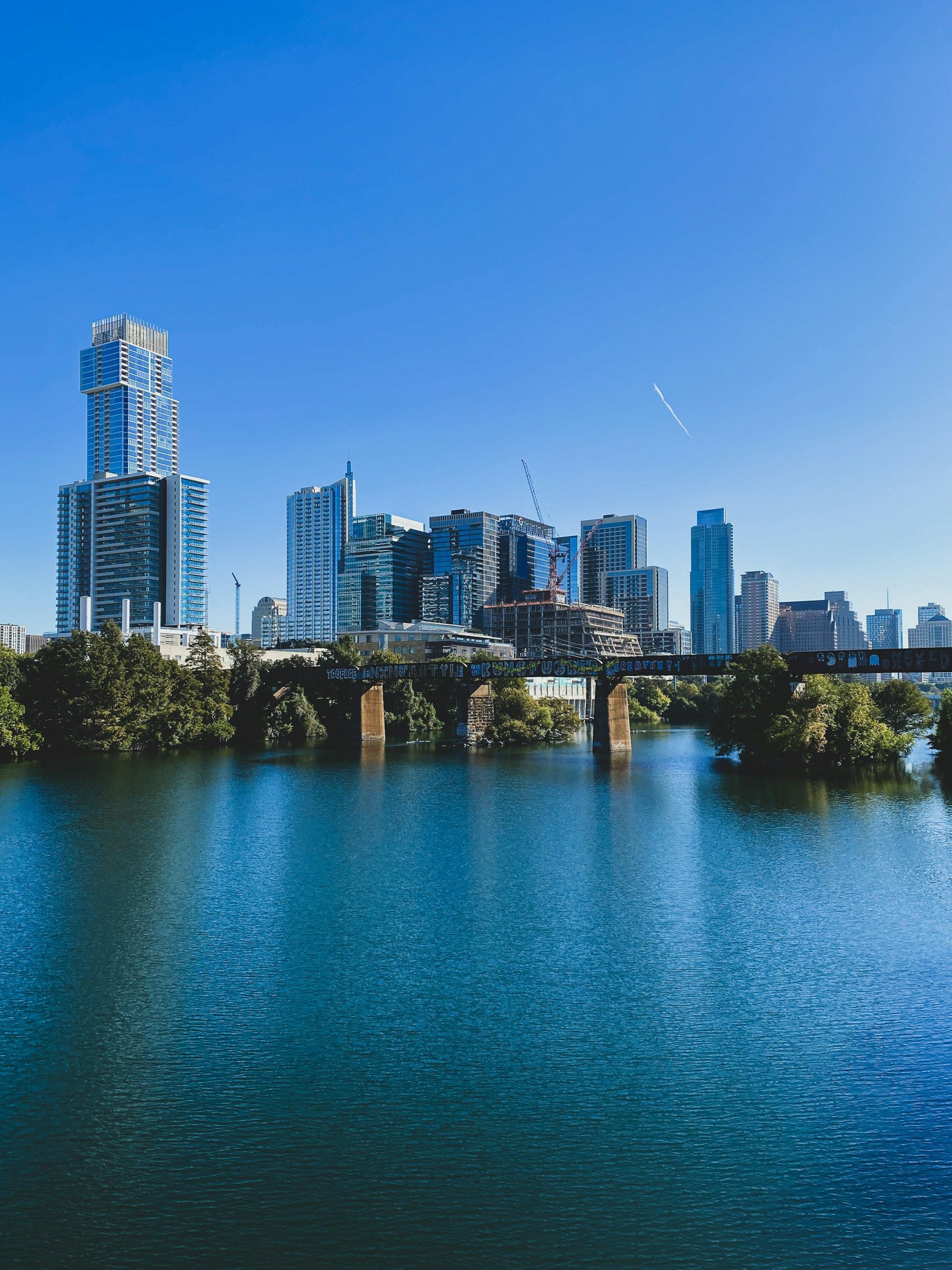 Austin, Texas skyline reflected in a blue river under a bright, cloudless sky.