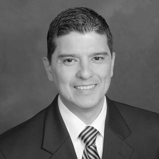 Man in suit smiling, with dark hair, looking at the camera.