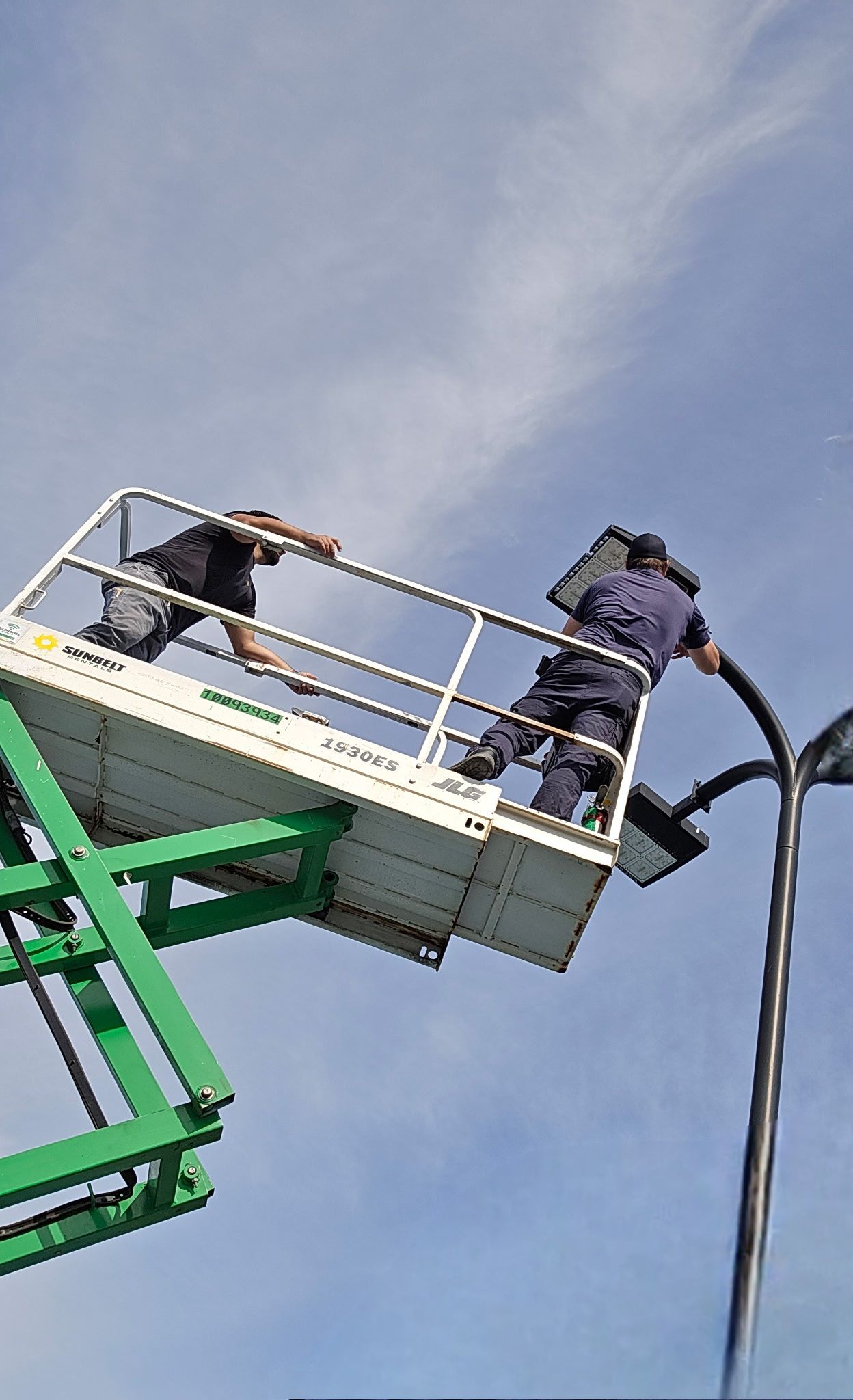 Two men are working on a street light on a crane.