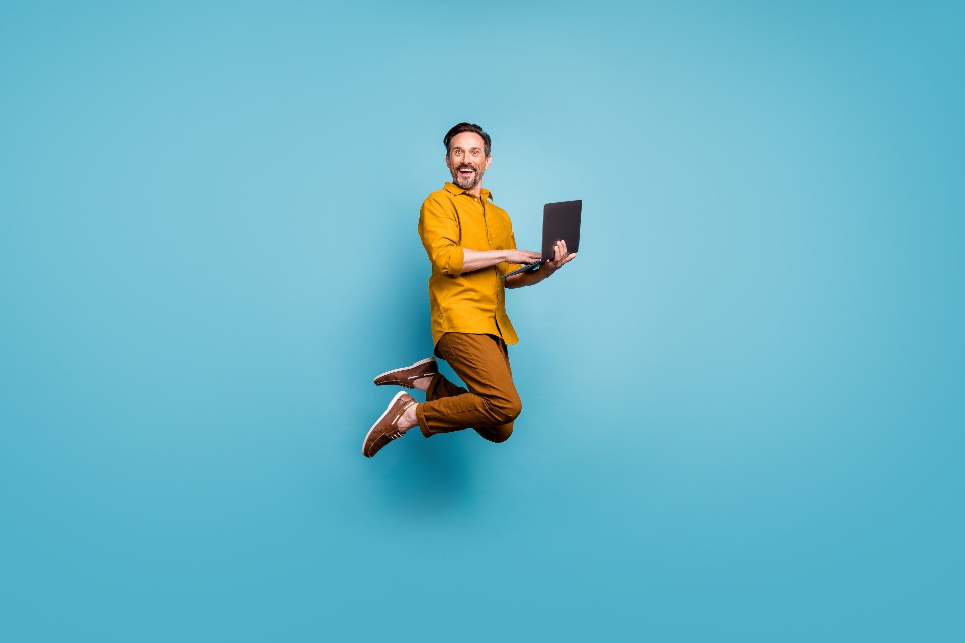 man jumping with laptop with smile on face