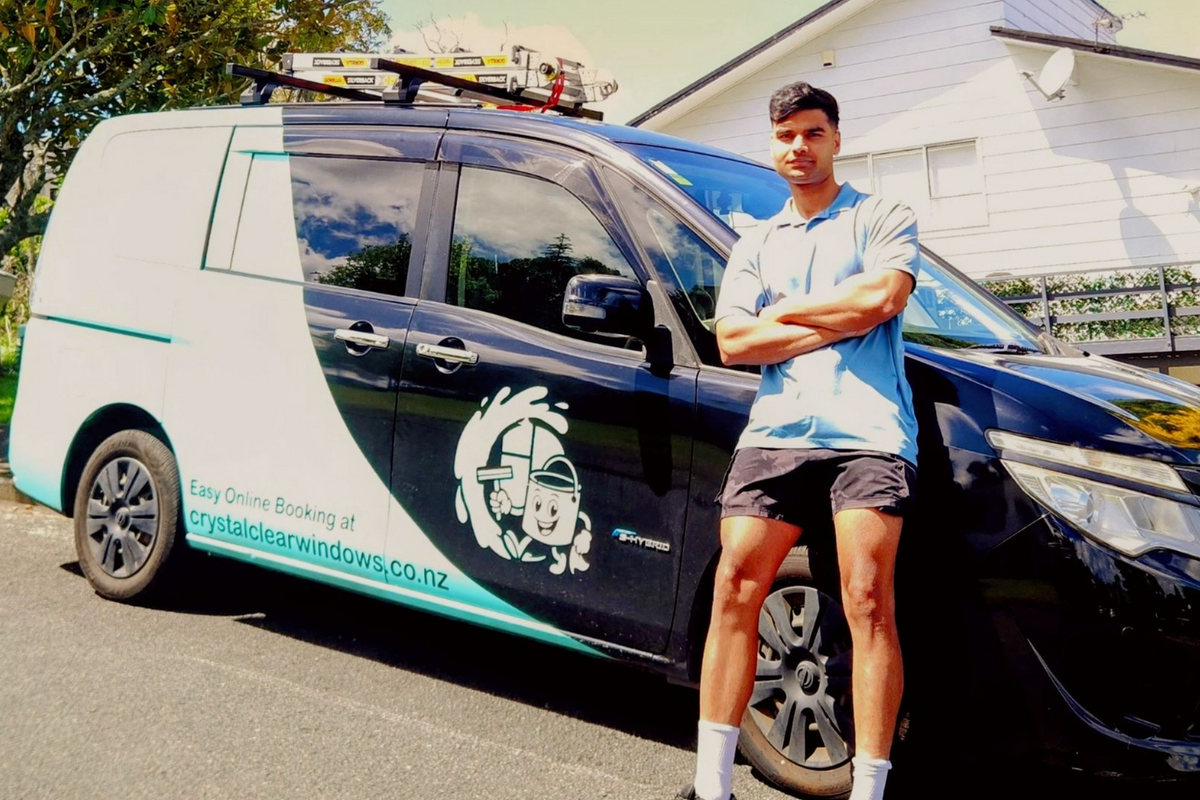 Man stands with arms crossed by his work van, which has a logo and company name.