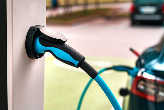 Gloved hand turning a control knob on a wall-mounted electrical device with a cable