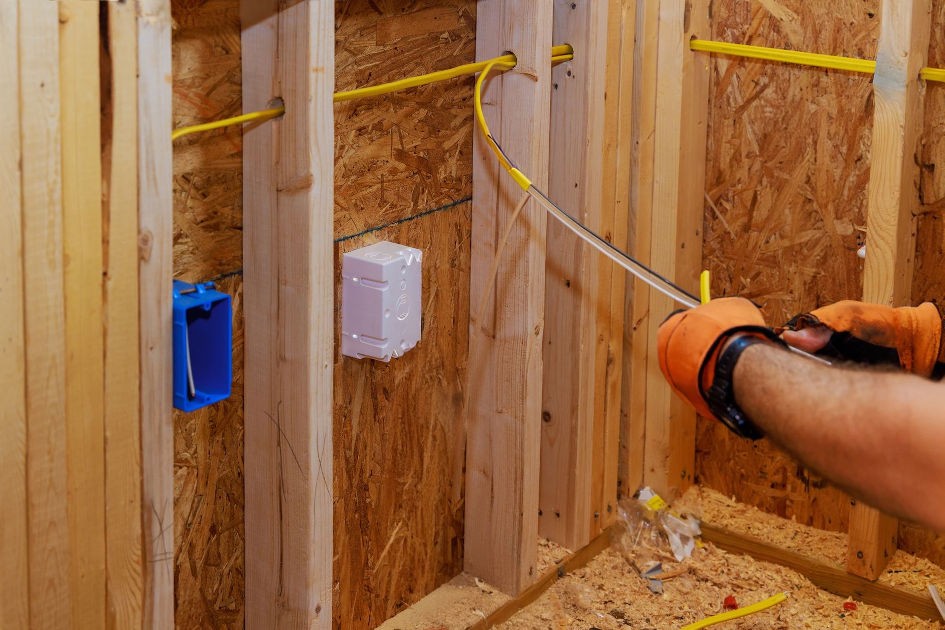 Hand installing electrical wiring and outlet boxes inside a framed wall during construction