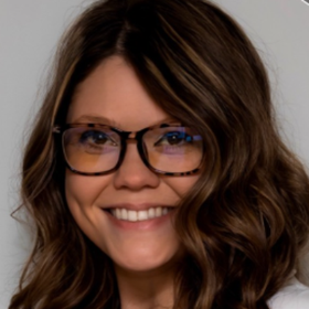 Woman with brown hair and glasses smiles.