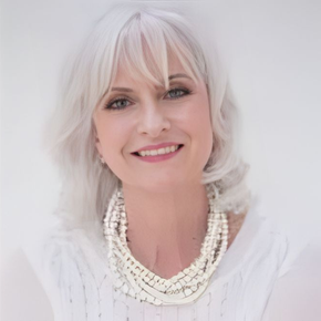 Woman with silver hair smiles, wearing pearl necklace and white top.