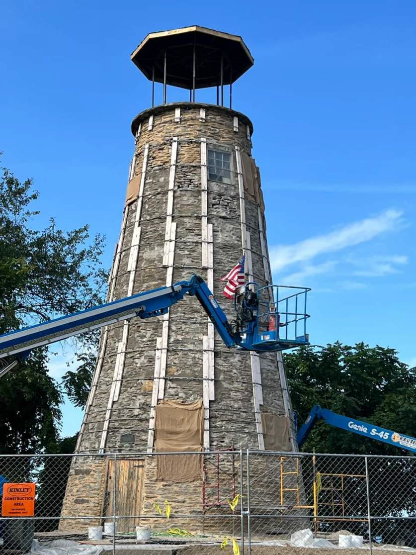 A man on a crane is working on a large stone tower.