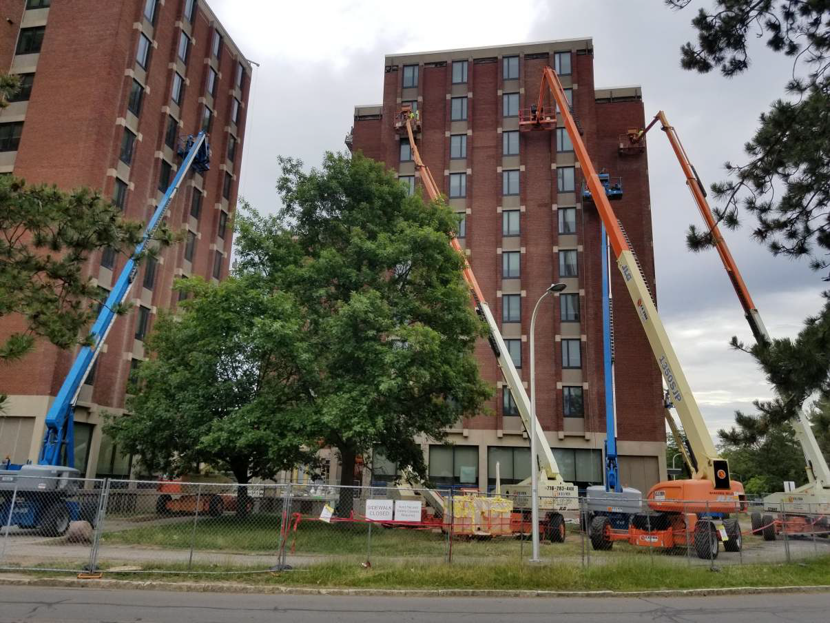 A row of construction vehicles are parked in front of a tall building.