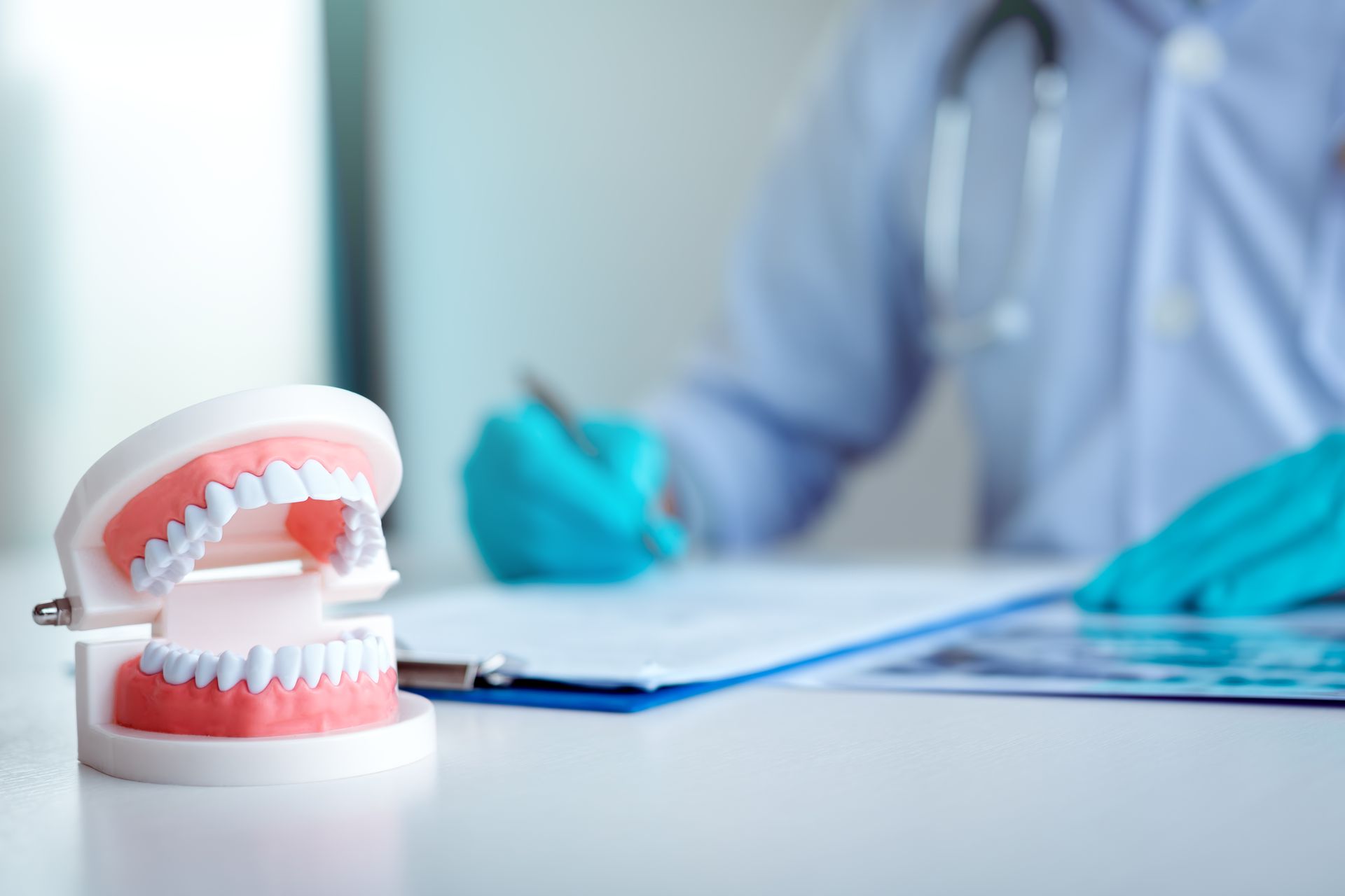 Dental model on a desk with a dentist reviewing patient charts in the background.