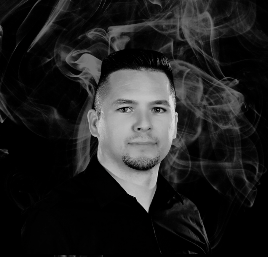 Man in black shirt, looking forward, with smoky background.